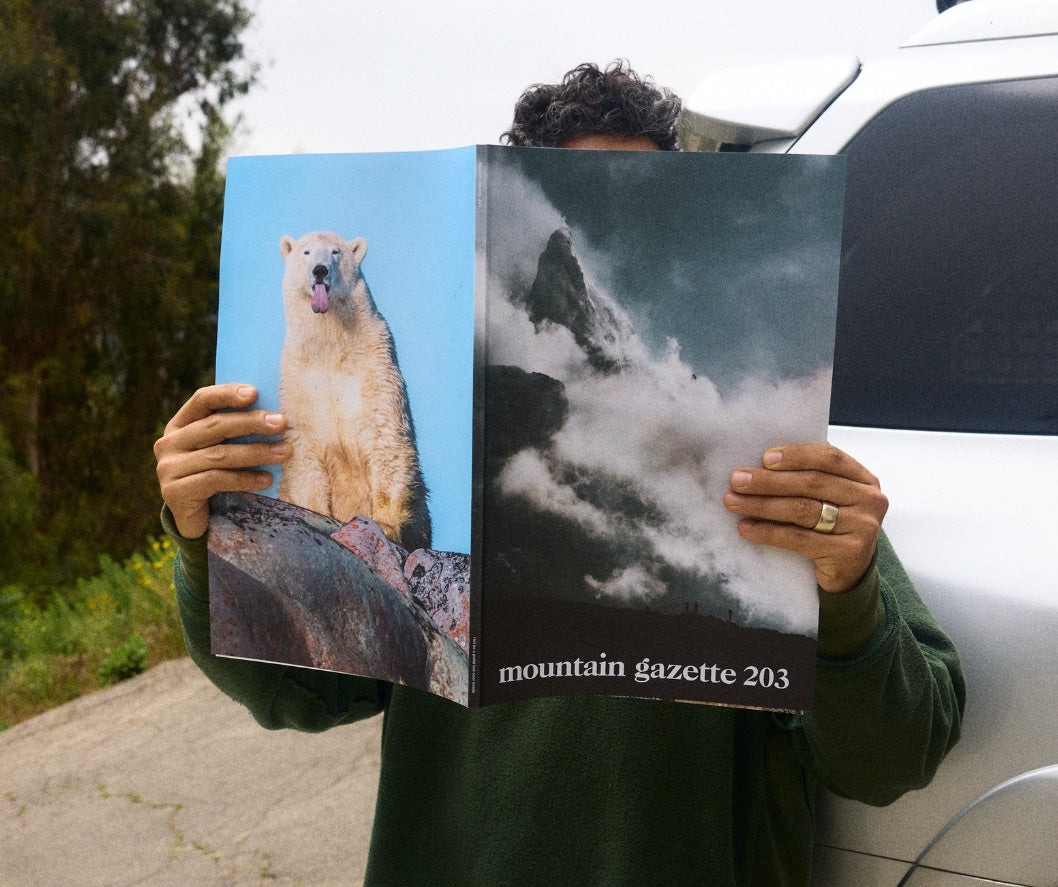 An man holding an open copy of Mountain Gazette magazine issue 203 the spring issue. The front cover shows a mountain and the back a polar bear